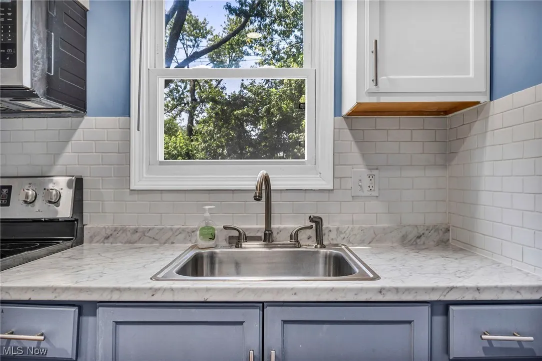 Kitchen with stainless steel microwave, range, light countertops, backsplash, and plenty of natural light