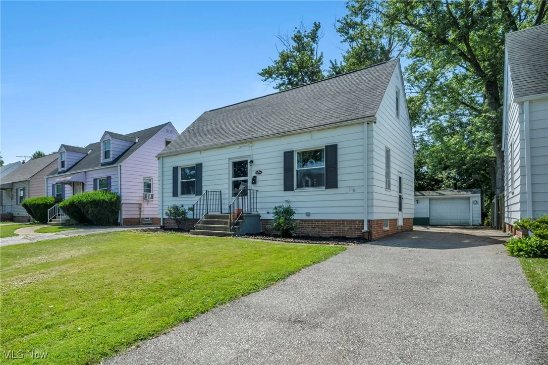 Cape cod-style house featuring an outbuilding, entry steps, roof with shingles, driveway, and a front lawn