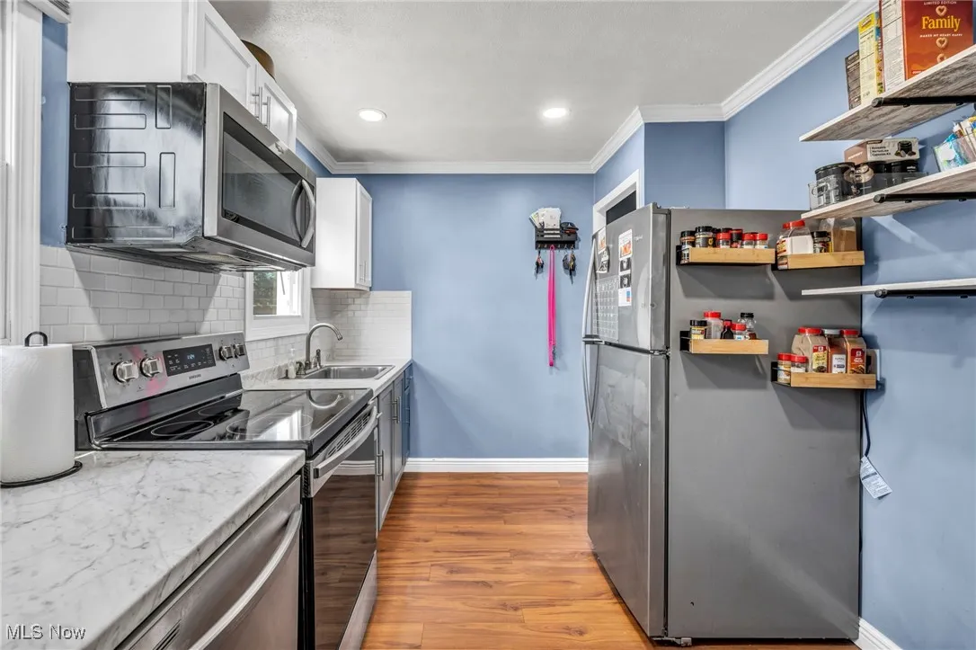 Kitchen featuring stainless steel appliances, crown molding, tasteful backsplash, white cabinets, and light wood-style floors