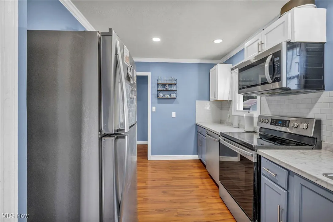 Kitchen featuring stainless steel appliances, wood finished floors, tasteful backsplash, crown molding, and recessed lighting