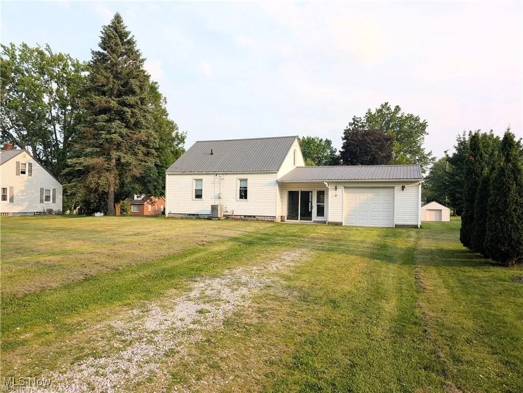 Rear view of house featuring driveway, an attached garage, a metal roof, and a lawn