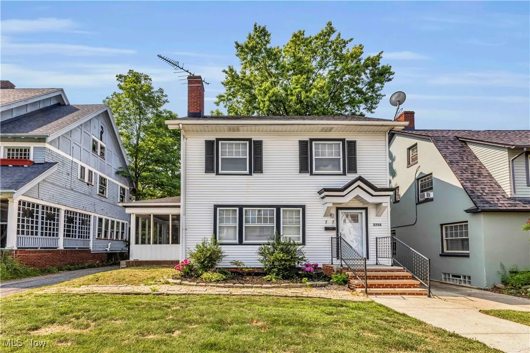 View of front of property featuring a chimney, a sunroom, and a front lawn