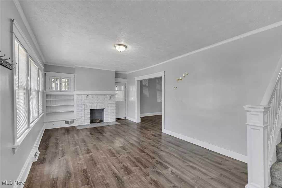 Unfurnished living room featuring a fireplace, a textured ceiling, wood finished floors, stairway, and crown molding