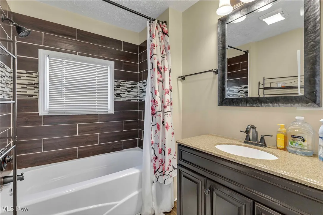Full bathroom with shower / bathtub combination with curtain, vanity, and a textured ceiling