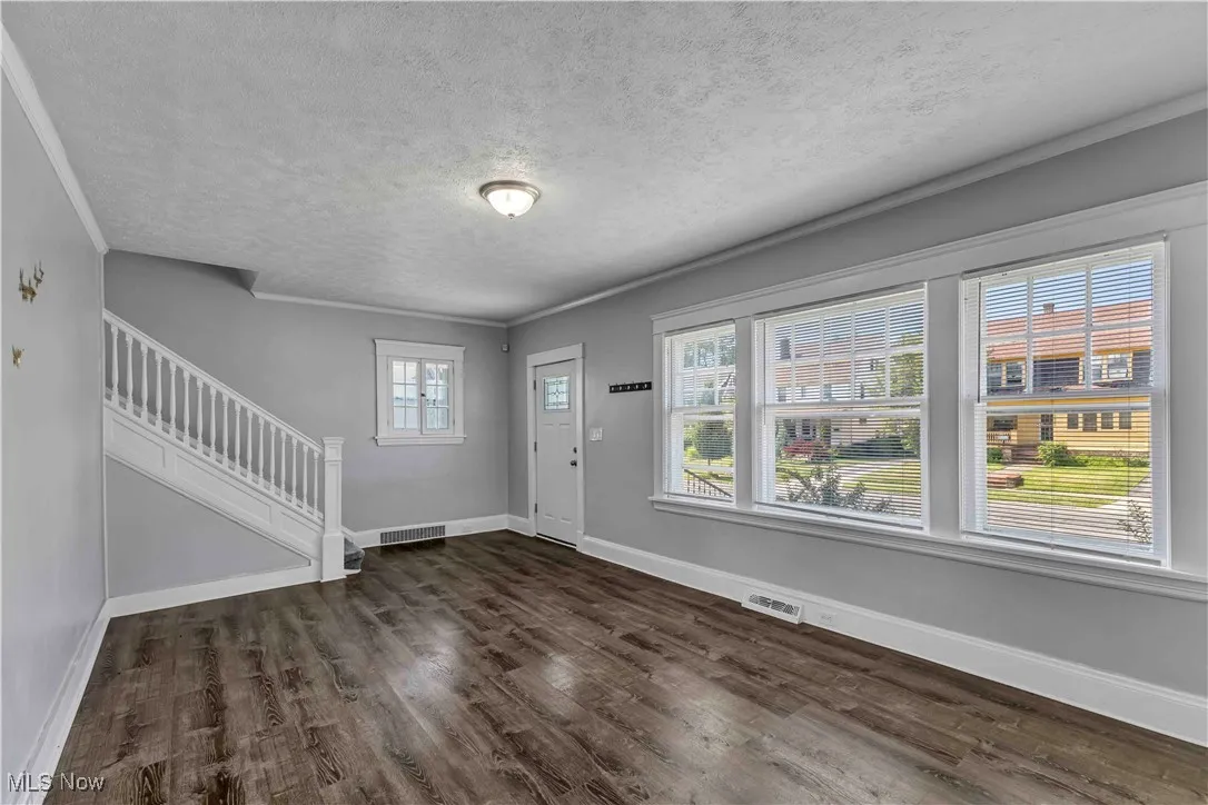 Entrance foyer featuring a textured ceiling, dark wood finished floors, stairs, and crown molding