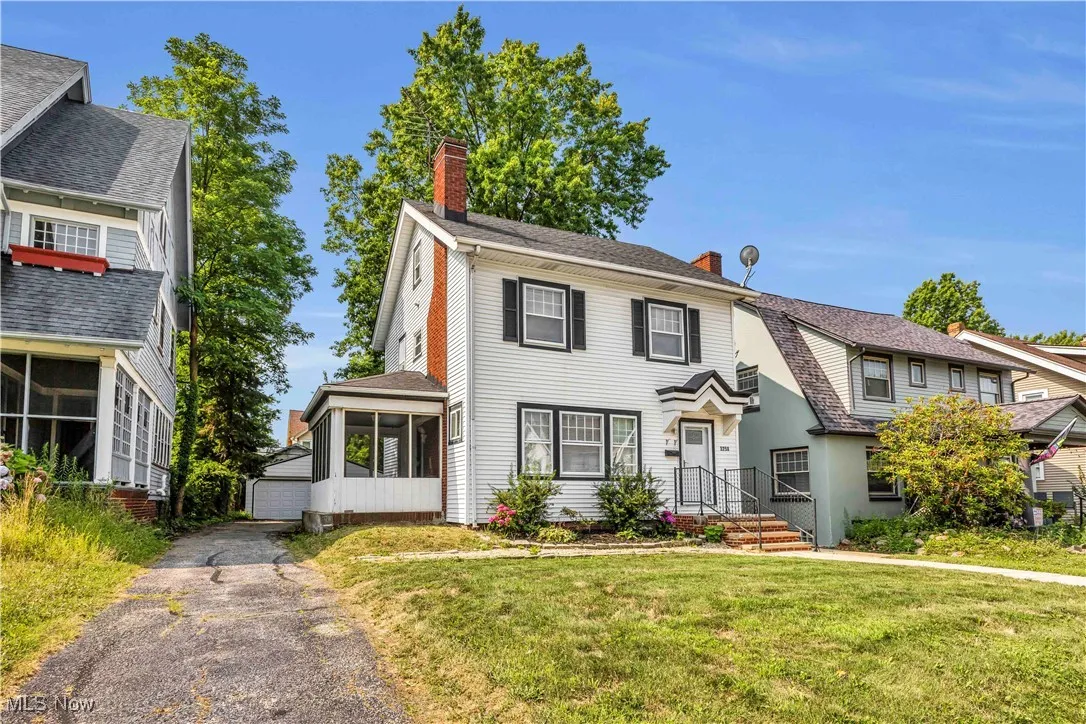 View of front of home featuring a chimney, a sunroom, an outbuilding, and a front yard