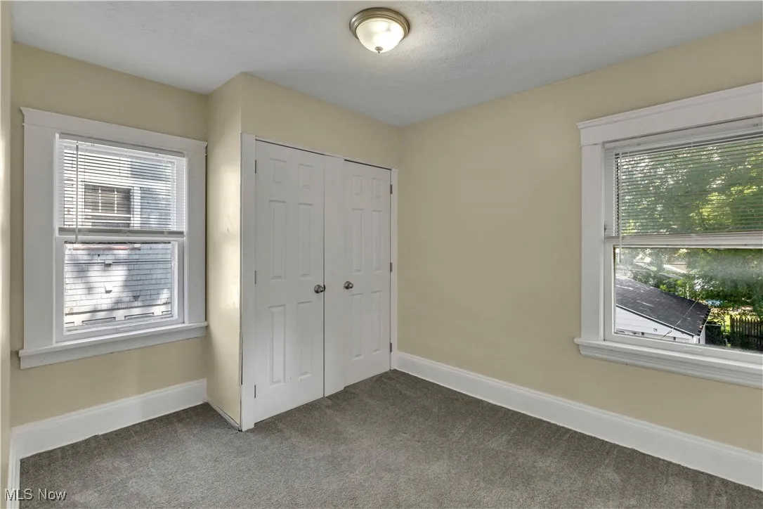 Unfurnished bedroom featuring dark colored carpet, multiple windows, a closet, and a textured ceiling