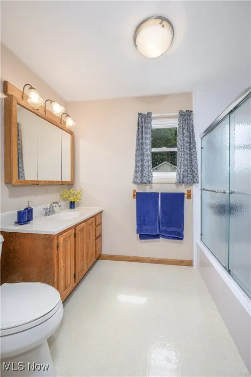 Bathroom featuring vanity, bath / shower combo with glass door