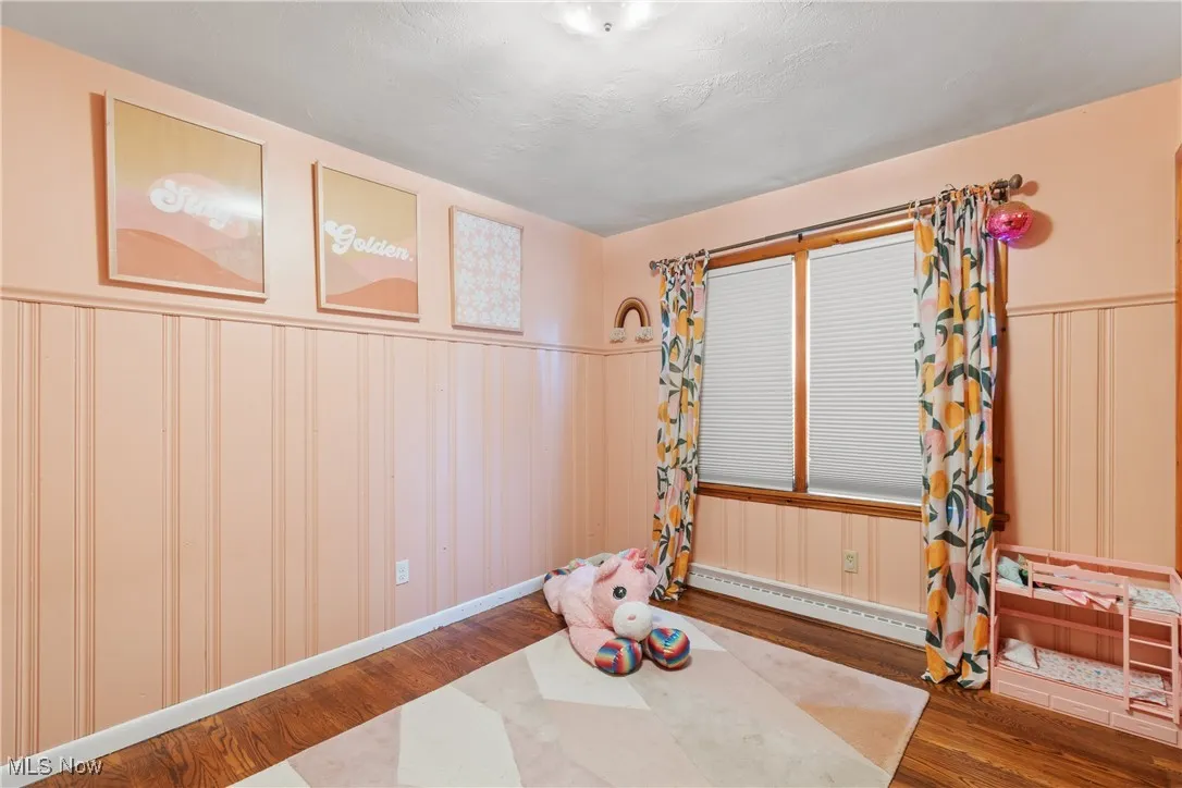 Unfurnished room featuring wood finished floors, a wainscoted wall, a baseboard heating unit, and a decorative wall