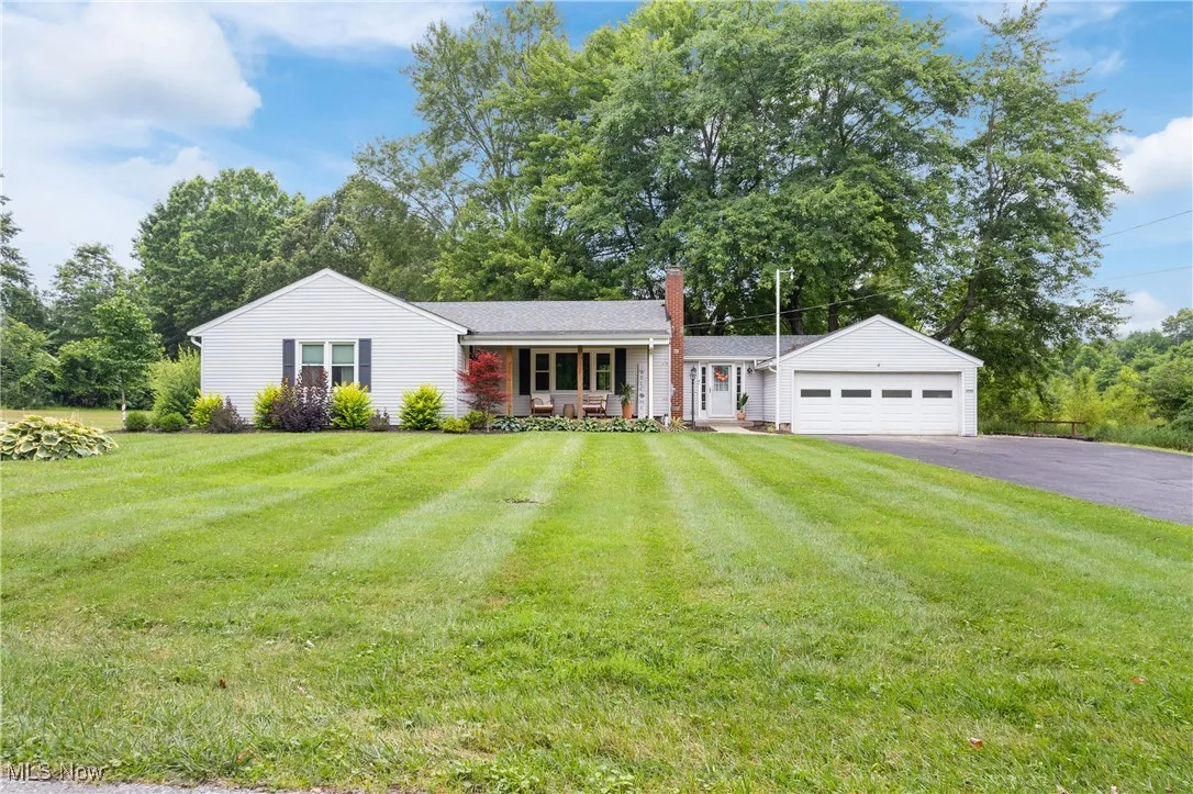 Single story home with driveway, covered porch, a front yard, a garage, and a chimney