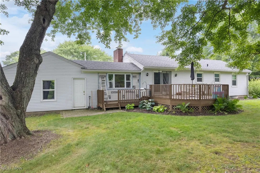 Rear view of house featuring a chimney, a deck, a yard, and roof with shingles