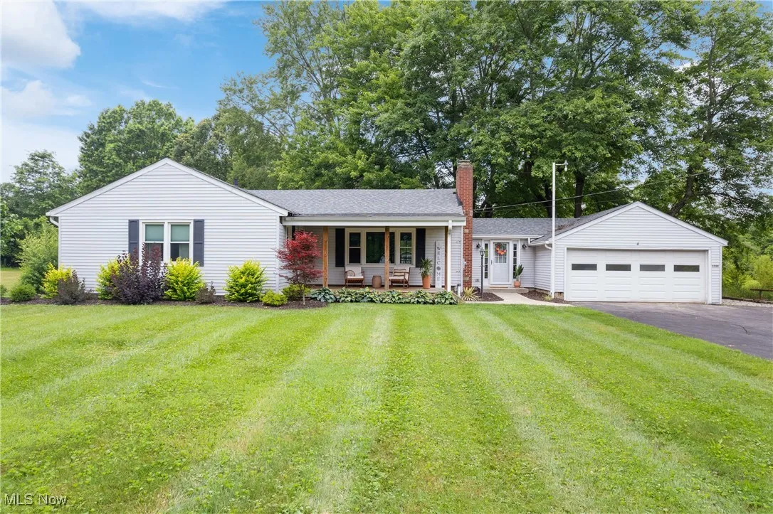 Ranch-style house with a porch, asphalt driveway, a chimney, an attached garage, and a front lawn