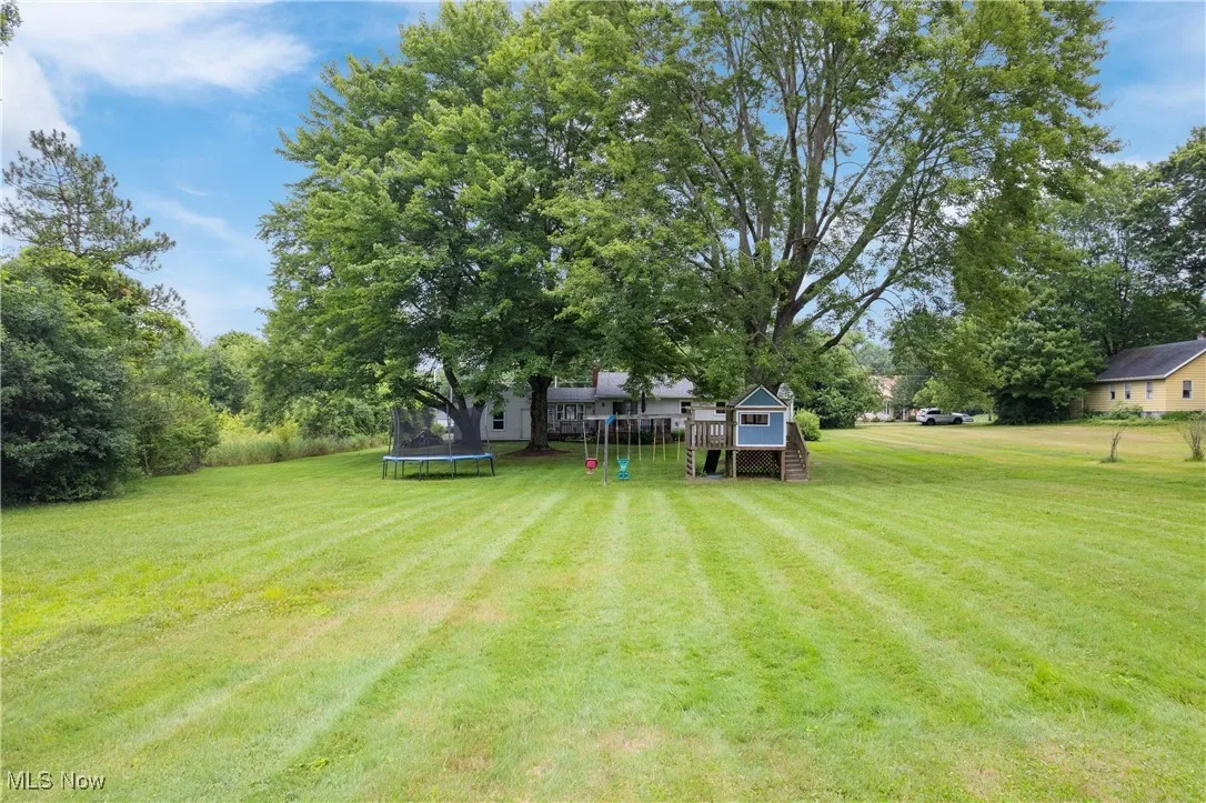 View of grassy yard with a trampoline and a deck