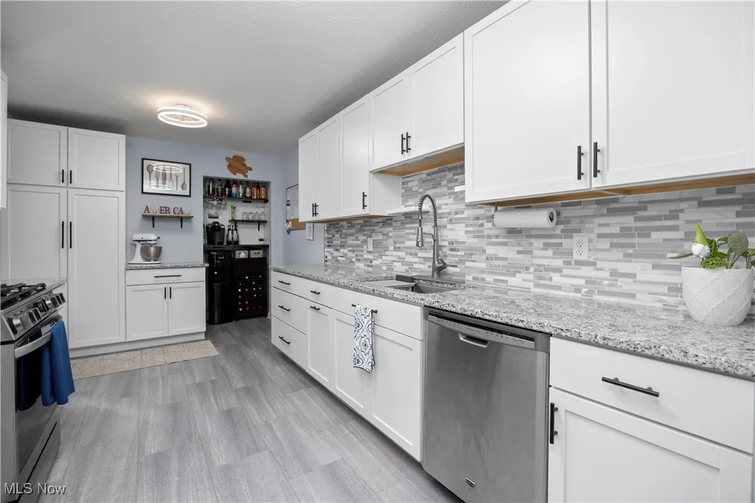 Kitchen featuring appliances with stainless steel finishes, white cabinets, tasteful backsplash, light stone countertops, and light wood-type flooring