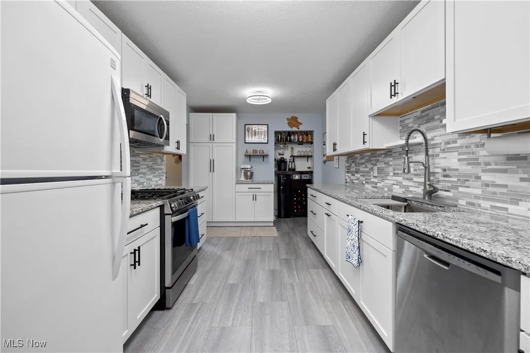 Kitchen with stainless steel appliances, decorative backsplash, white cabinets, light stone counters, and a textured ceiling