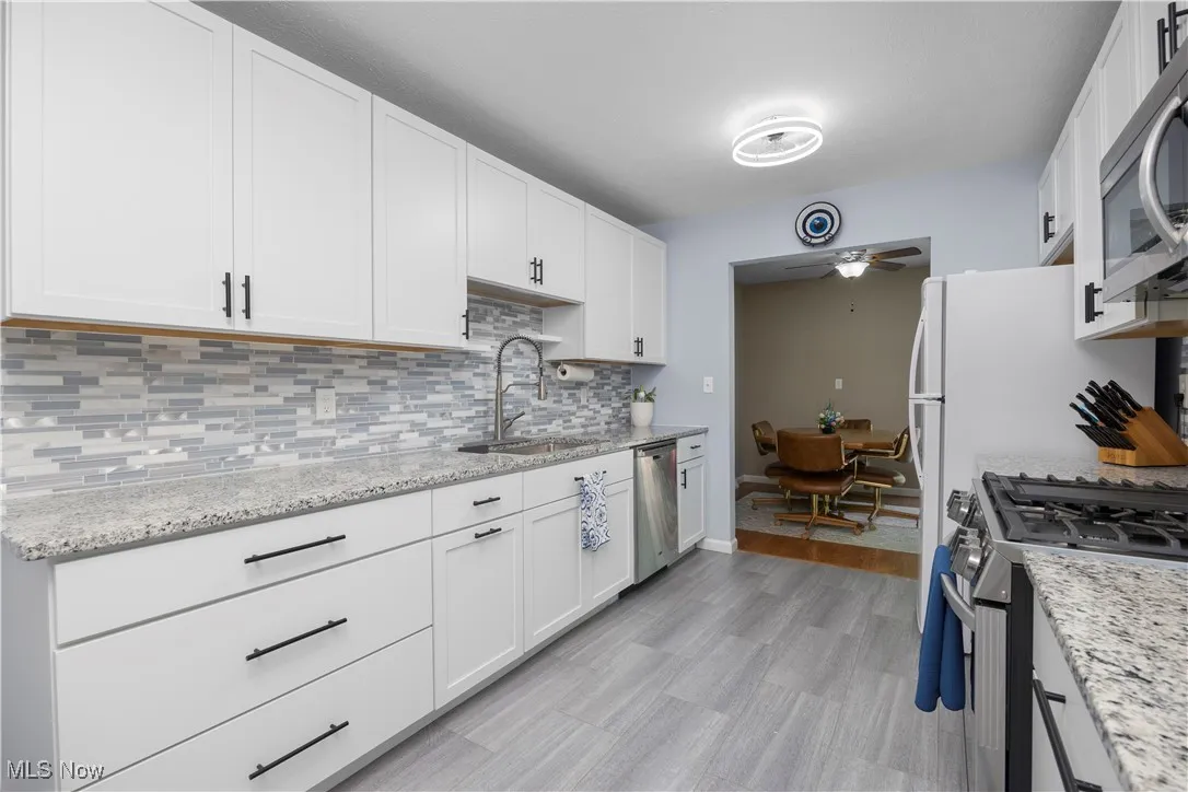 Kitchen featuring appliances with stainless steel finishes, tasteful backsplash, ceiling fan, white cabinets, and light stone counters