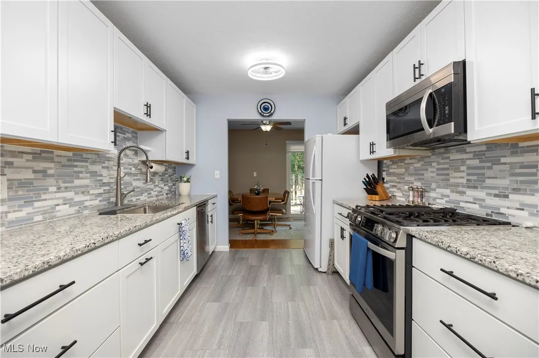 Kitchen with stainless steel appliances, a ceiling fan, white cabinetry, and tasteful backsplash