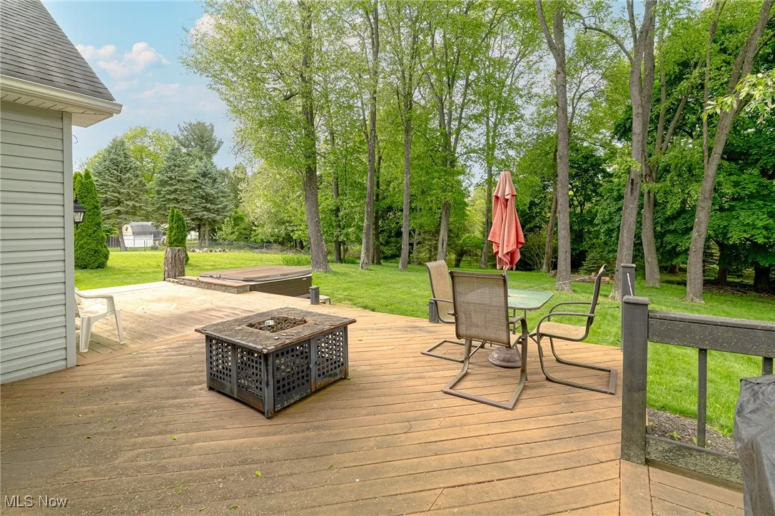 Wooden deck with an outdoor fire pit, a yard, outdoor dining area, and view of scattered trees