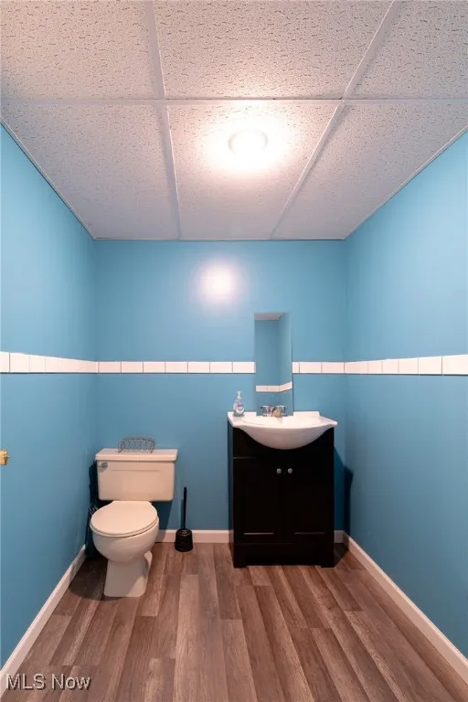 Half bath with vanity, wood finished floors, and a drop ceiling