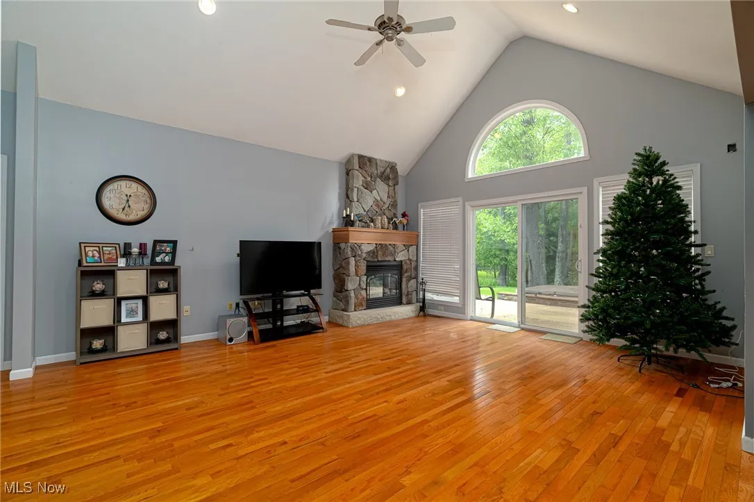 Living area with light wood-type flooring, high vaulted ceiling, a ceiling fan, a fireplace, and recessed lighting