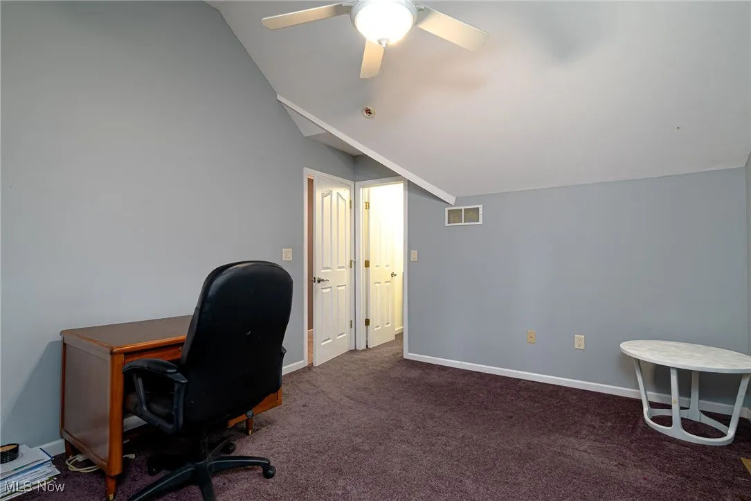 Carpeted home office with vaulted ceiling and ceiling fan