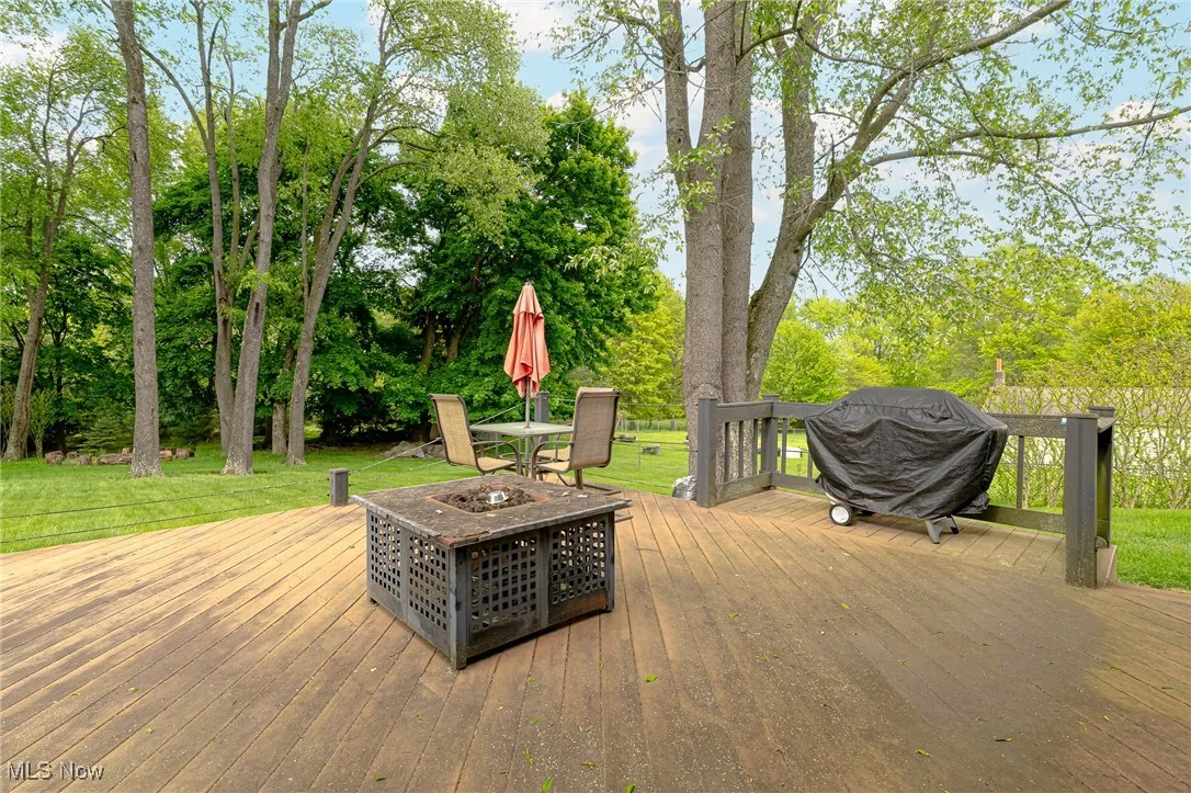Deck featuring an outdoor fire pit, view of wooded area, a lawn, and a grill
