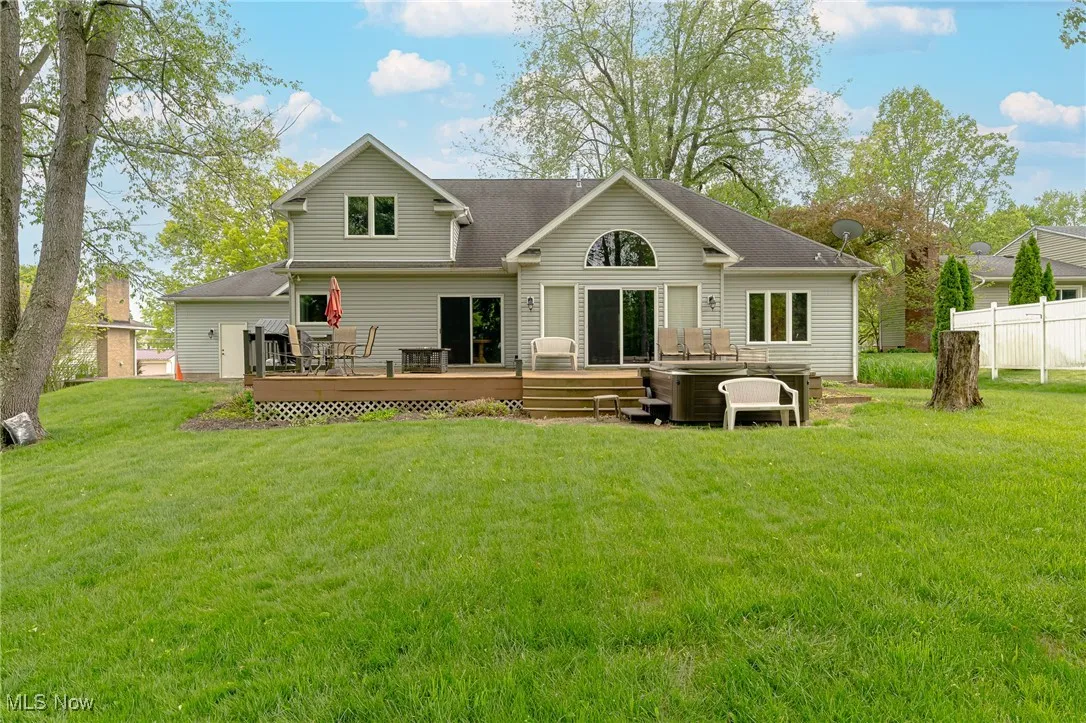 Back of house with a hot tub, a deck, and a shingled roof