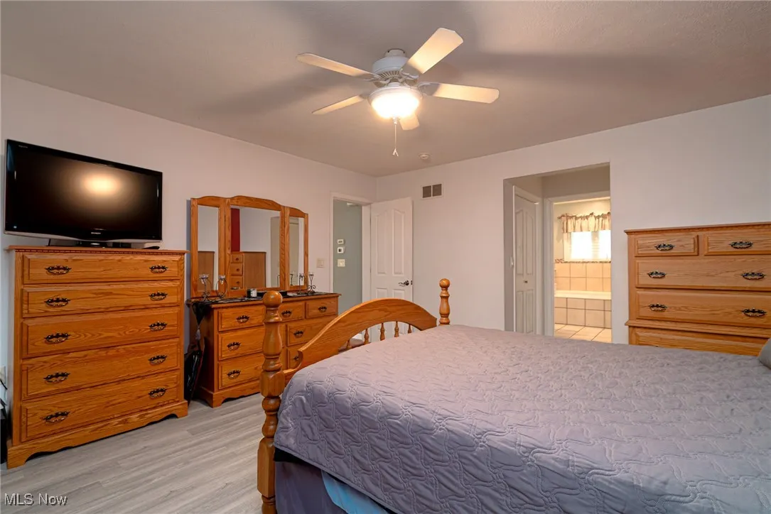 Bedroom with light wood finished floors, ceiling fan, and ensuite bathroom