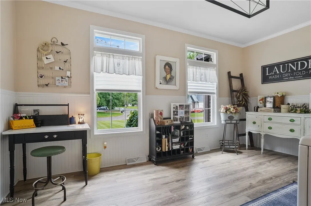 Office space featuring wainscoting, wood finished floors, healthy amount of natural light, and ornamental molding