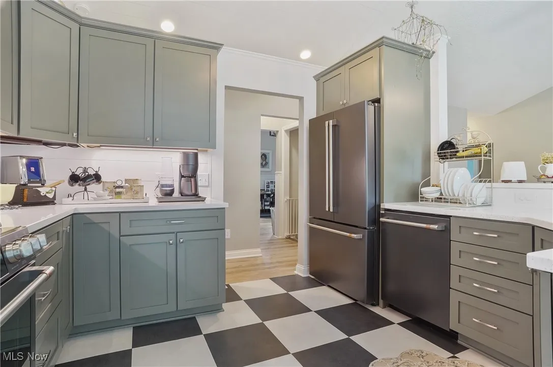 Kitchen with appliances with stainless steel finishes, light floors, light countertops, and ornamental molding