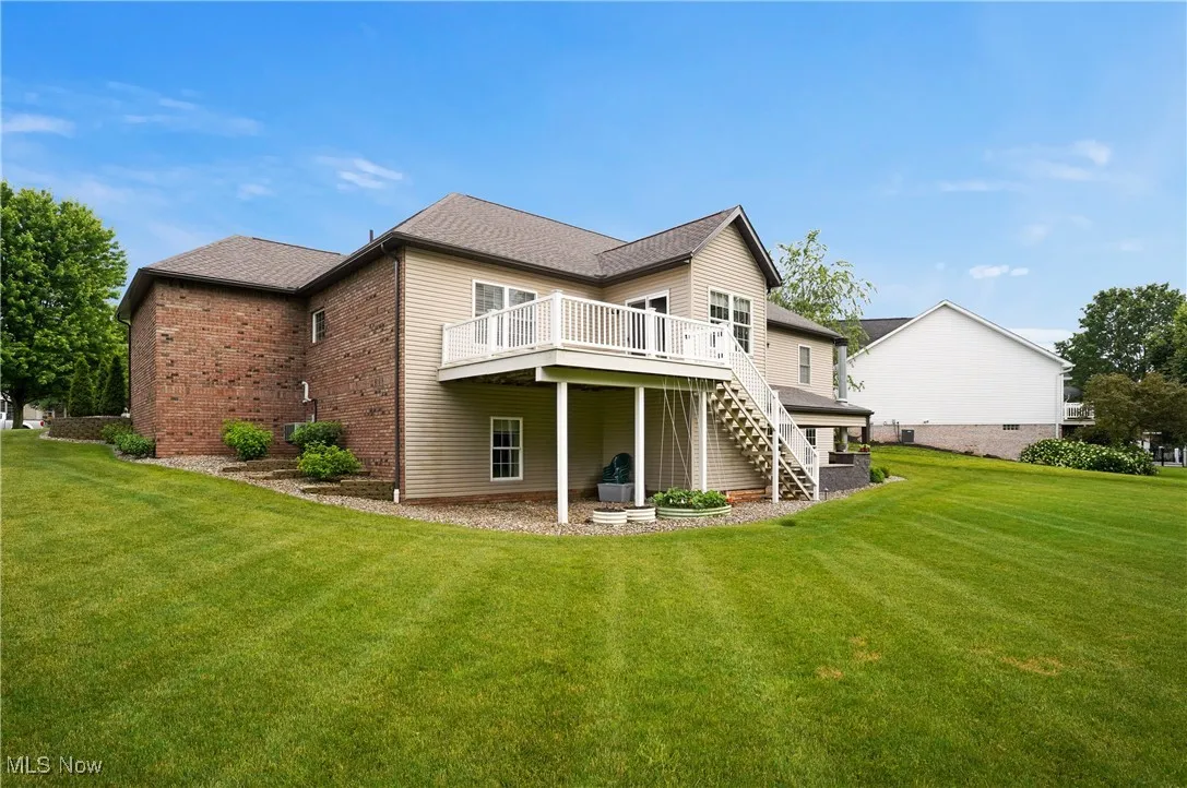 Back of property featuring stairway, a wooden deck, a lawn, and brick siding