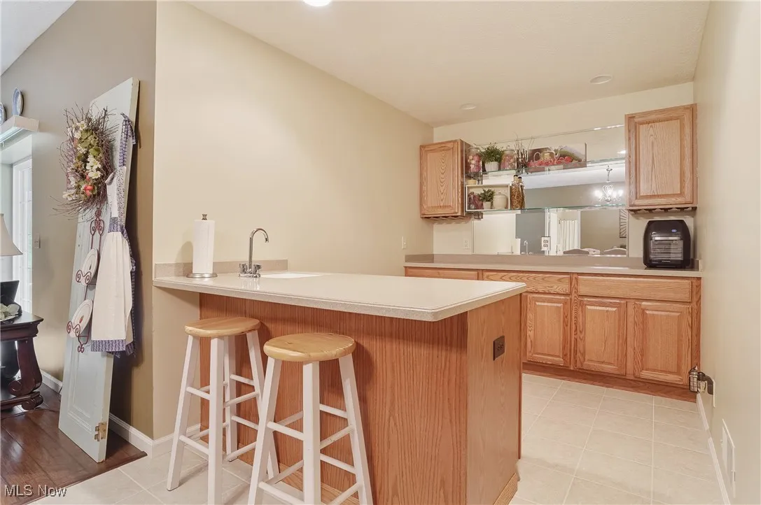 Kitchen with a peninsula, a kitchen breakfast bar, light countertops, open shelves, and light tile patterned flooring