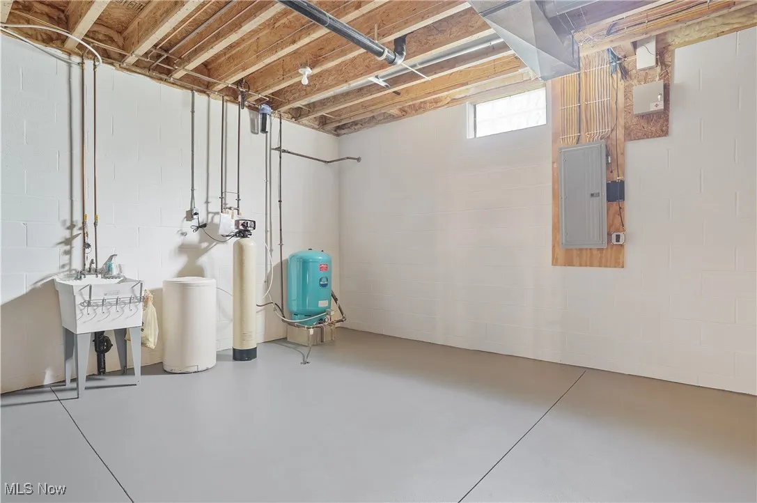 Below grade area with electric panel, a water softener, a water pressure tank, and concrete block wall