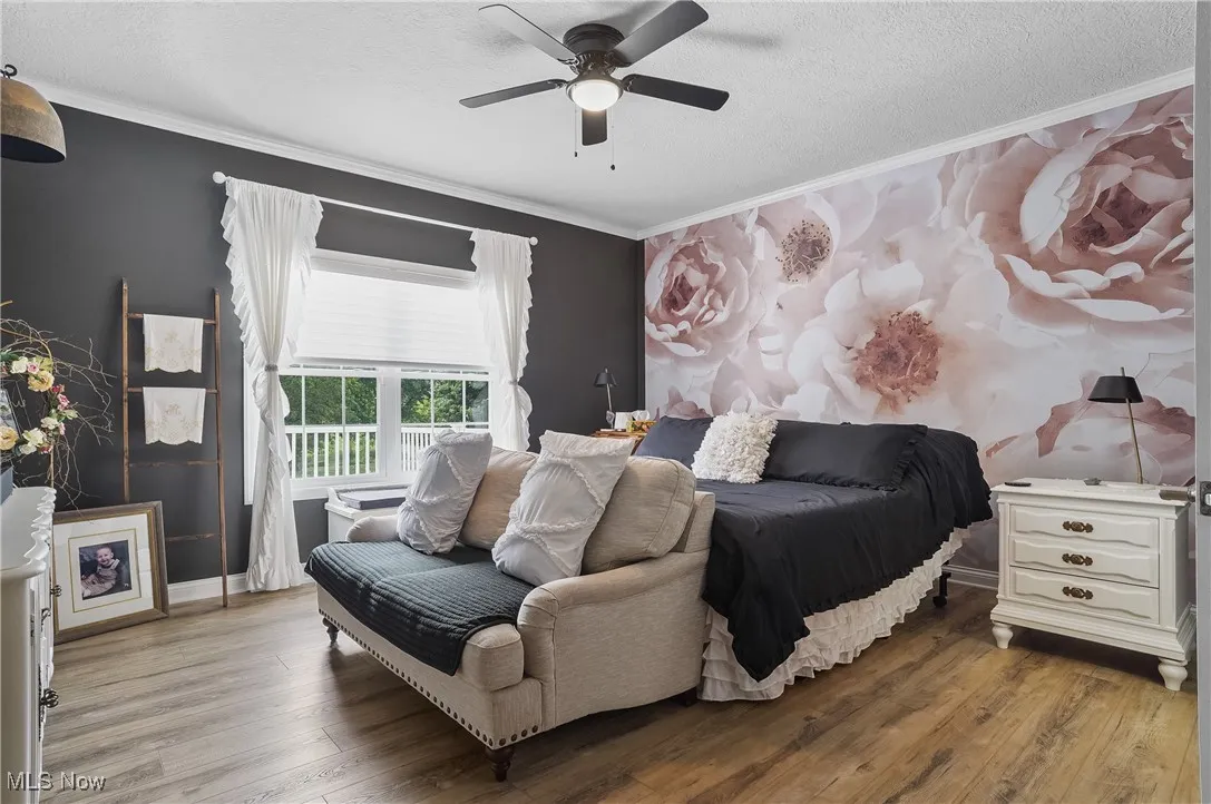 Bedroom featuring wood finished floors, crown molding, a textured ceiling, ceiling fan, and an accent wall