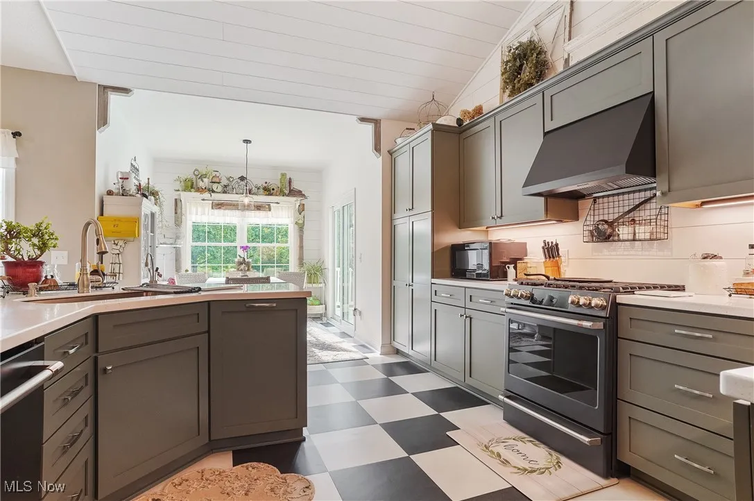 Kitchen featuring stainless steel appliances, range hood, light flooring, gray cabinetry, and vaulted ceiling