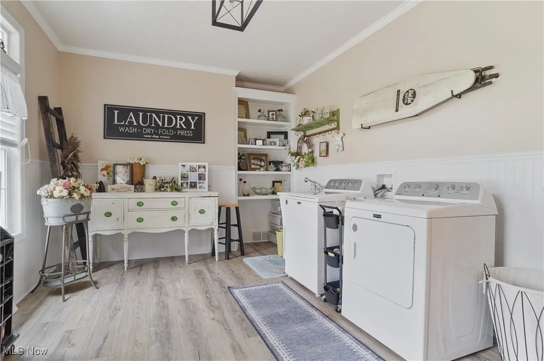 Laundry room with washer and clothes dryer, ornamental molding, wainscoting, and wood finished floors