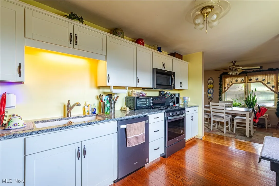 Kitchen with appliances with stainless steel finishes, ceiling fan, white cabinets, light wood finished floors, and stone counters