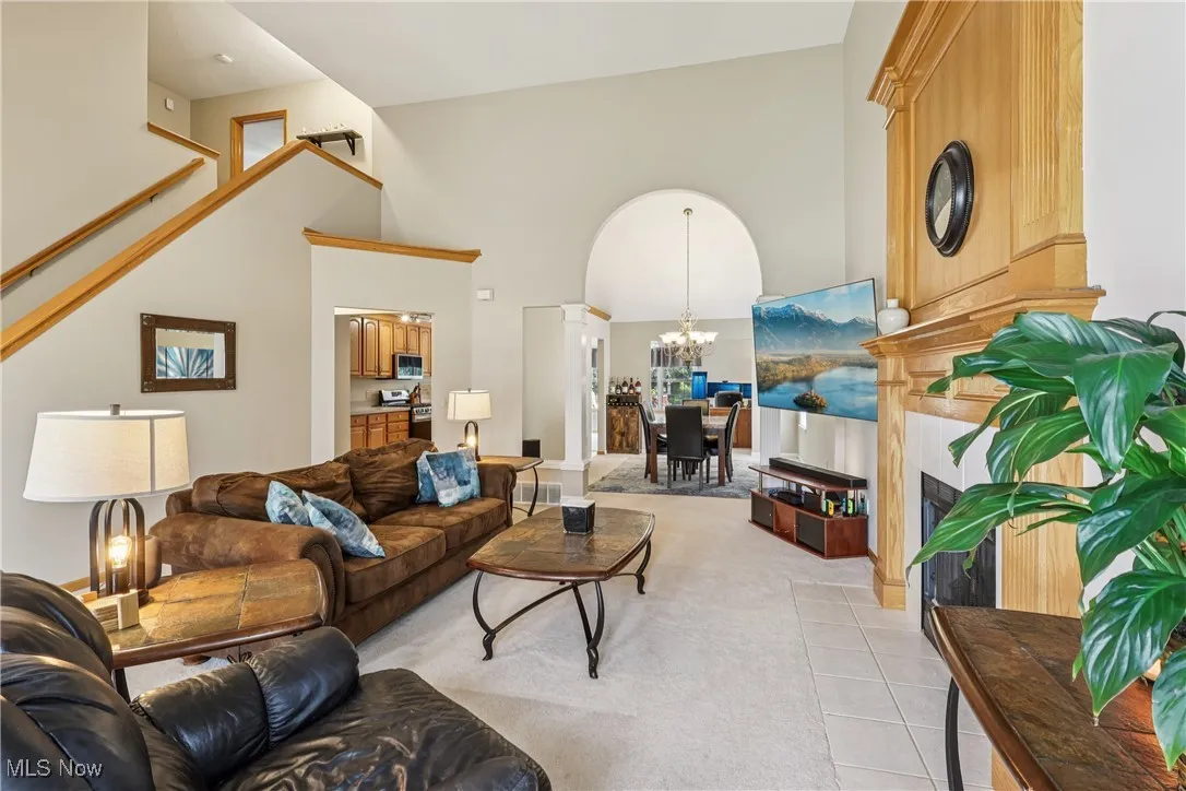 Living area featuring a chandelier, light tile patterned flooring, a fireplace, a high ceiling, and light carpet