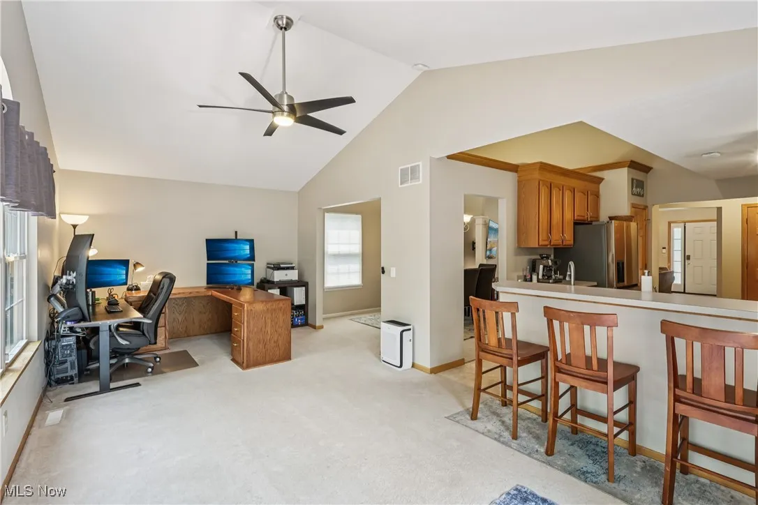 Sunroom with vaulted ceiling, ceiling fan / light and carpet flooring currently being used as an office