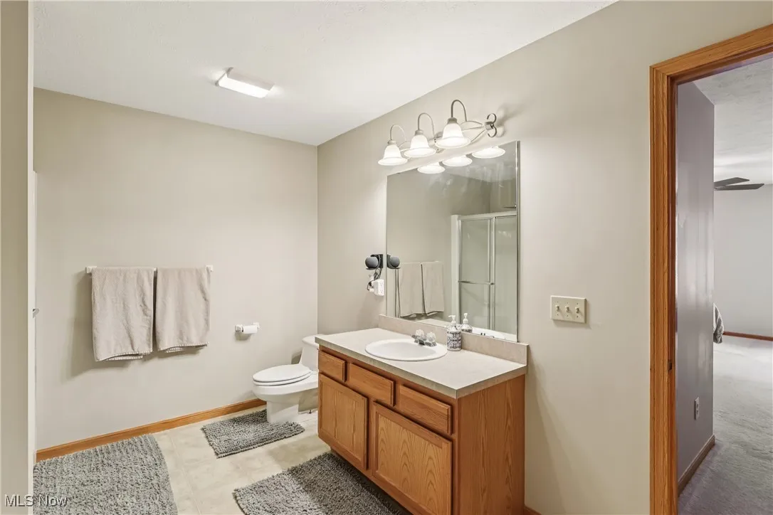 First floor primary bathroom with sink, vanity special lighting, commode and tile flooring