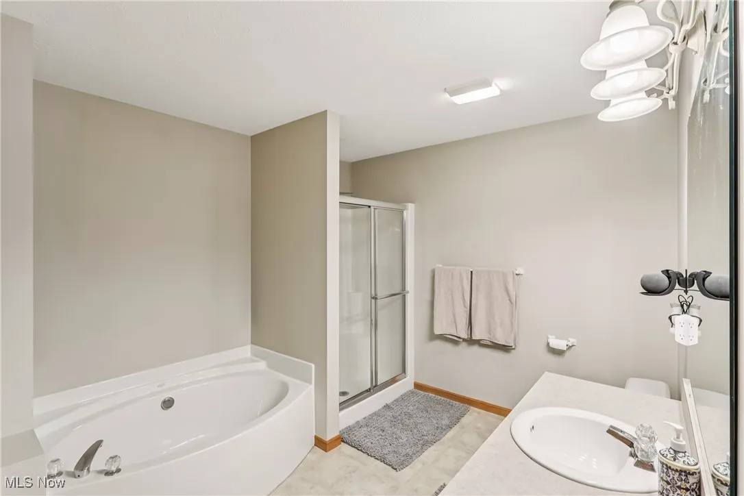 First floor primary bathroom with sink, vanity, special lighting, jetted tub, shower stall, commode and tile flooring