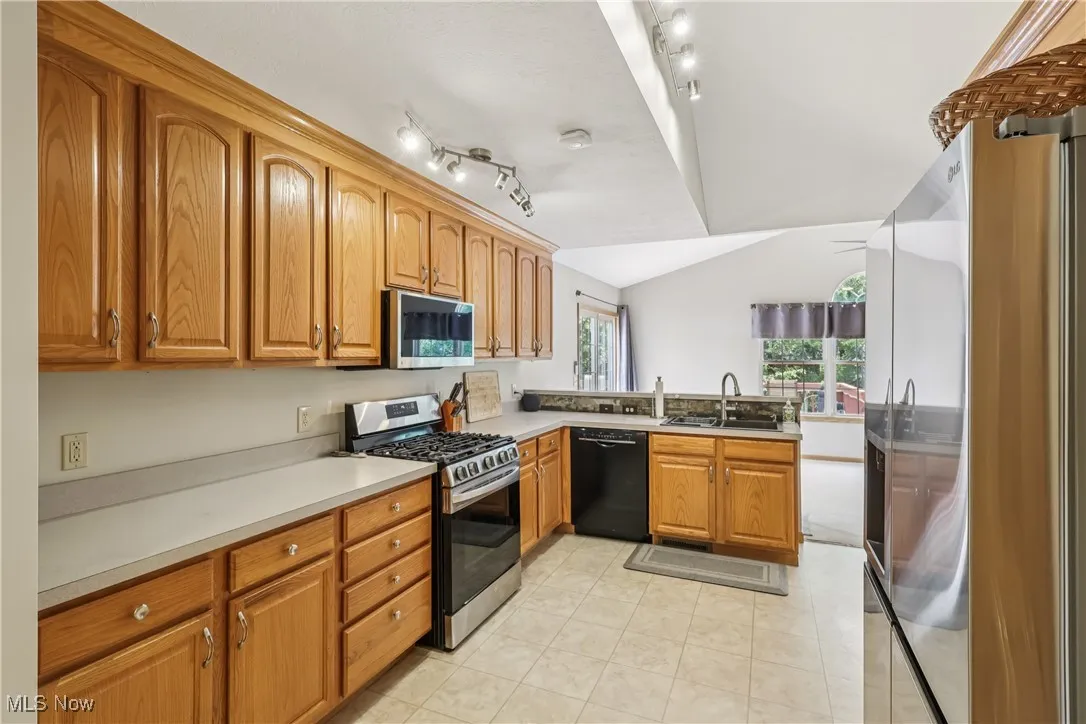 Kitchen featuring vaulted ceiling, recessed lighting, sink, dishwasher, stove, microwave, refrigerator, cupboards and plenty of counter space.