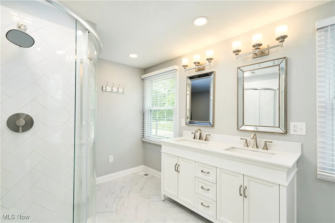 Full bath with a tile shower, double vanity, marble finish flooring, and recessed lighting