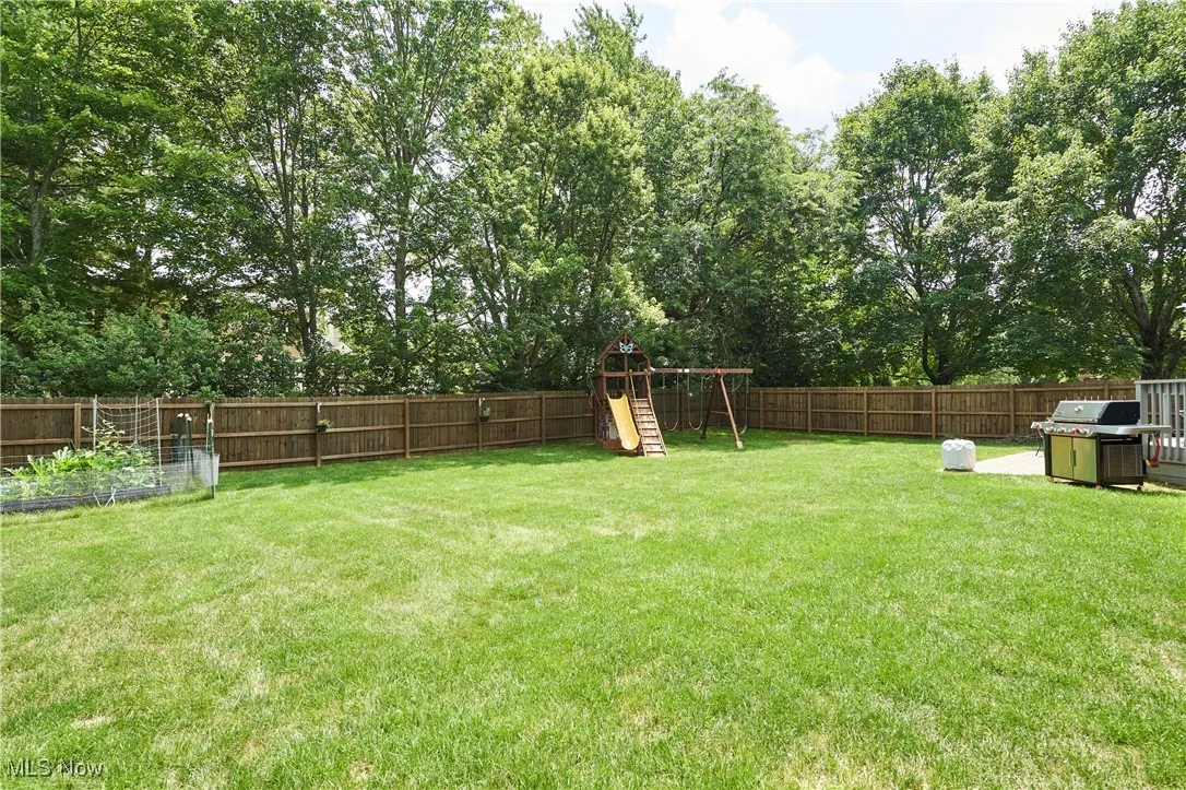 Fenced backyard featuring a playground, view of wooded area, and a garden