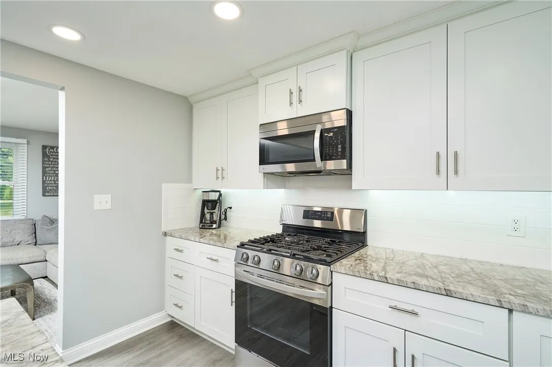 Kitchen featuring appliances with stainless steel finishes, light wood-style flooring, decorative backsplash, white cabinetry, and light stone counters