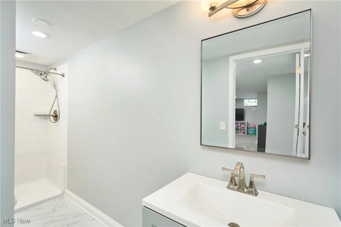 Bathroom featuring tiled shower, vanity, marble look tile flooring, and recessed lighting