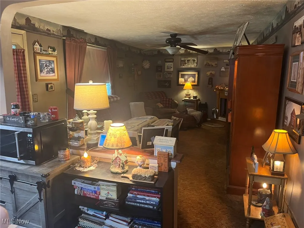 Living room featuring a ceiling fan, arched walkways, a textured ceiling, and carpet floors