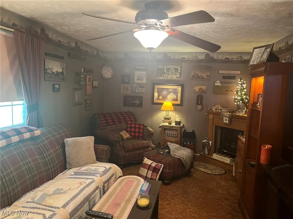 Carpeted living area with a textured ceiling, a ceiling fan, and a fireplace