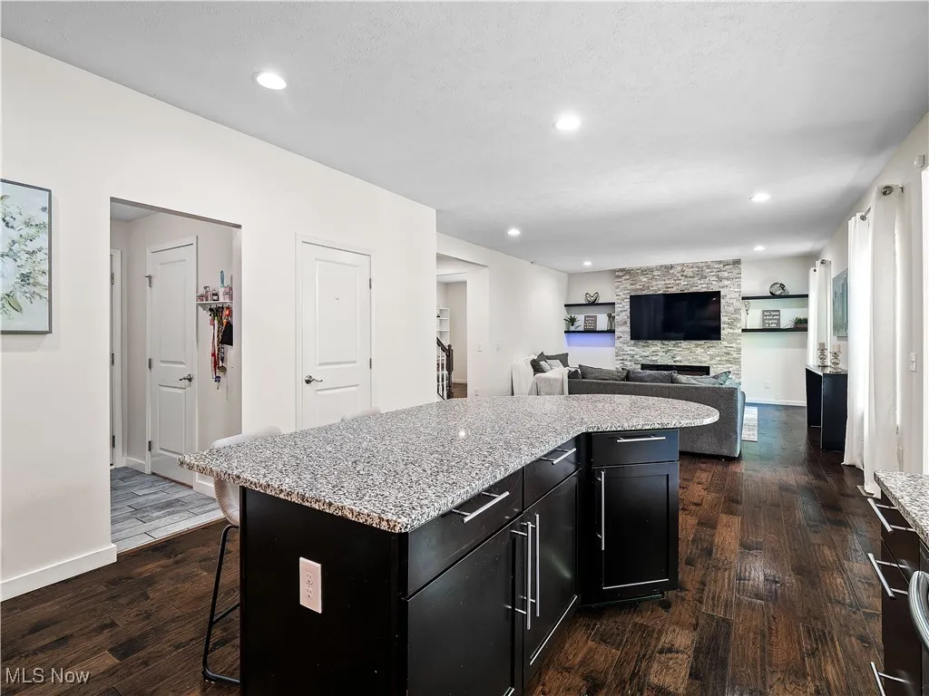 Kitchen with dark cabinets, dark wood-style flooring, a breakfast bar area, recessed lighting, and a kitchen island