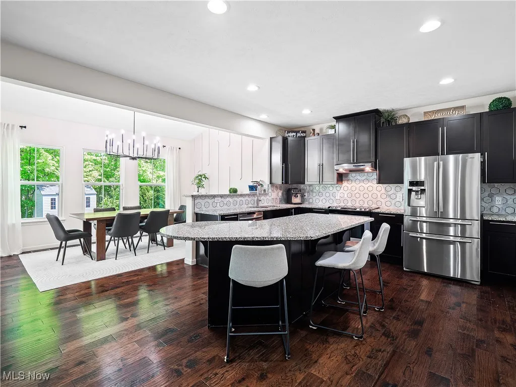 Kitchen with stainless steel fridge, a center island, light stone countertops, a kitchen breakfast bar, and under cabinet range hood